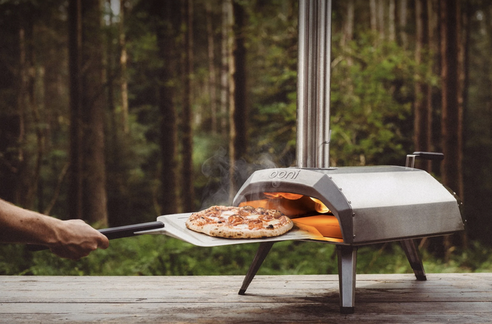 A metal pizza oven with a pizza being pulled out, perfectly cooked.
