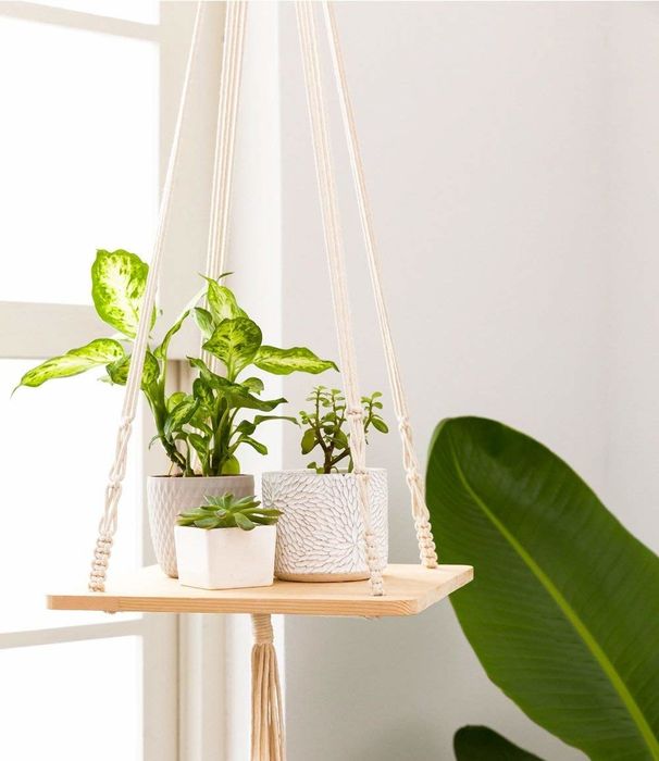 A wooden shelf suspended by white macrame, with a decorative tassel hanging beneath.