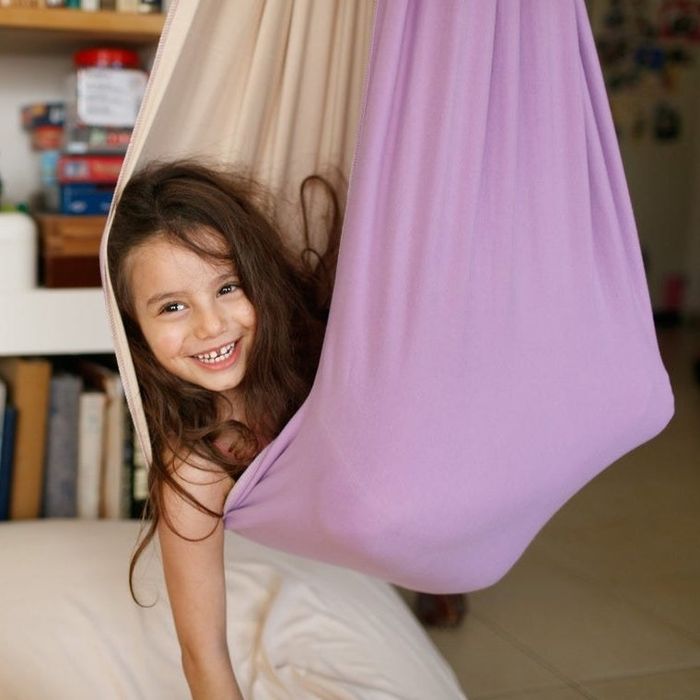 A child smiling with joy while curled up in a cozy hanging fabric chair