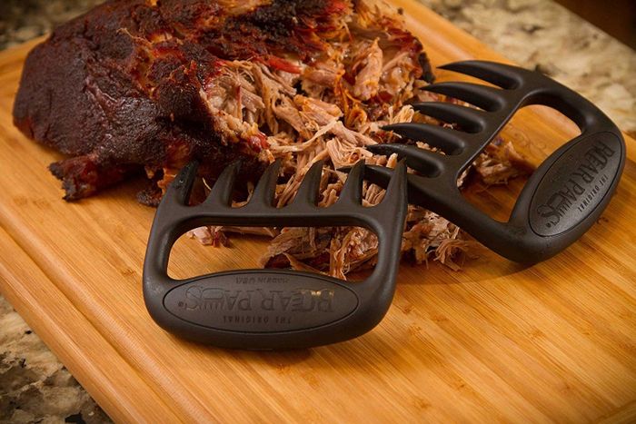 The black, claw-like meat shredders beside a piece of meat.