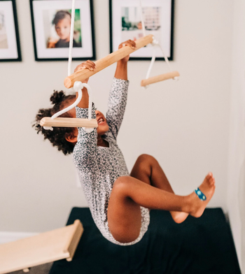 A child gripping the trapeze bar with both hands while hanging