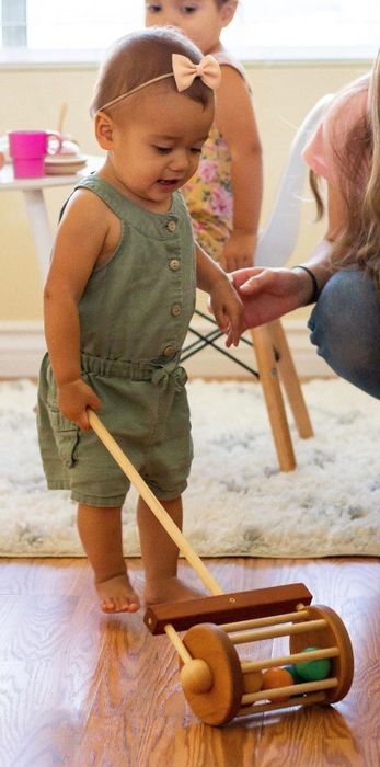 A small toddler happily pushing the lawnmower toy around.