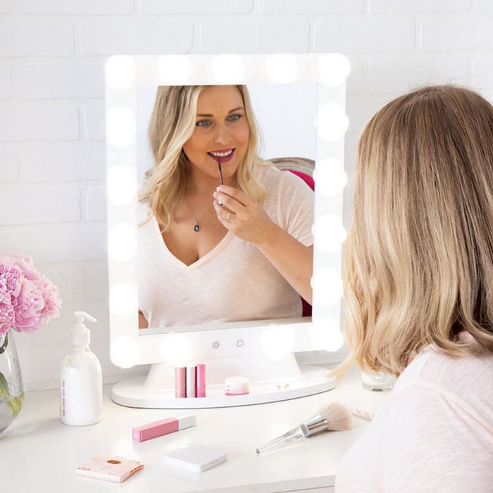 A model applying lipstick in front of the elegant white mirror.