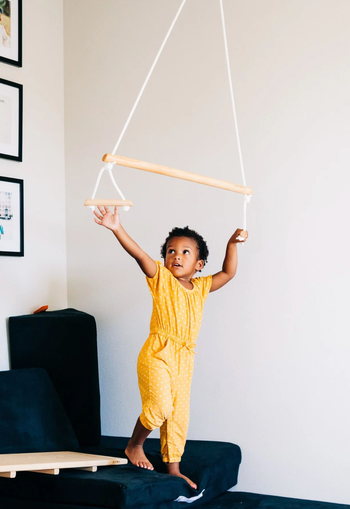 A child reaching up to grab the handles at each end of the trapeze bar