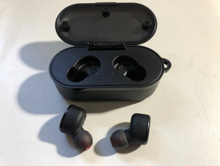 A reviewer’s image showing two black earbuds beside their charging case.