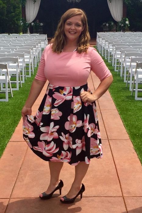 A reviewer is wearing a dress featuring a pink top and a floral skirt.