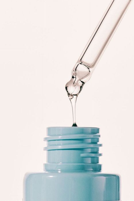 A dropper dispensing clear serum into a blue bottle