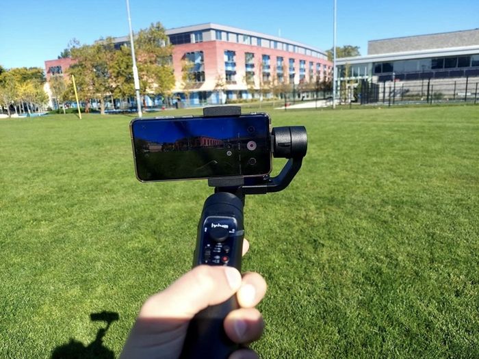 An iPhone positioned in the stabilizer, set against a park backdrop.