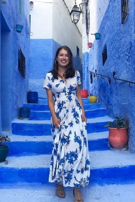 A reviewer wearing a short-sleeved white and blue dress, standing in a charming blue-painted alleyway.