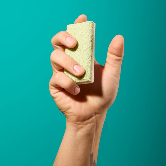 A hand pressing a green pumice stone against a solid teal background.