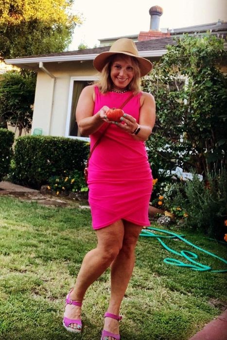 A reviewer dons the dress in a lovely pink shade, enjoying the tranquility of a backyard setting.
