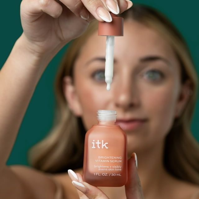 A woman holds a dropper and bottle of ITK's brightening serum, focusing on the product