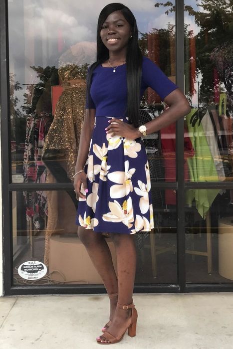 A reviewer is seen wearing a midi dress with three-quarter sleeves and a floral pattern on the skirt.