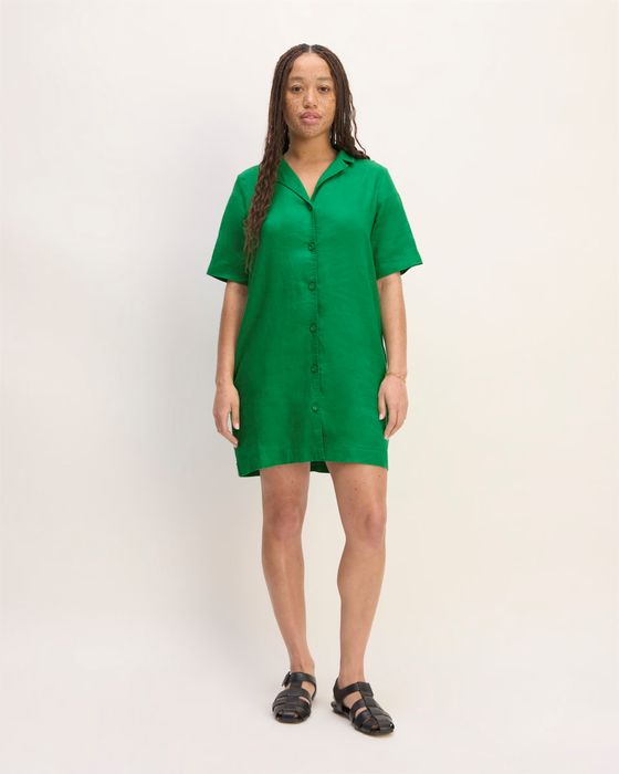 A woman models a short-sleeve, green button-down dress paired with black sandals, standing against a simple backdrop.