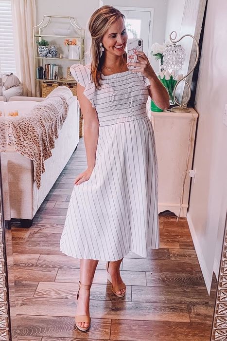 A reviewer in a white striped sundress takes a mirror selfie in a beautifully decorated living room.