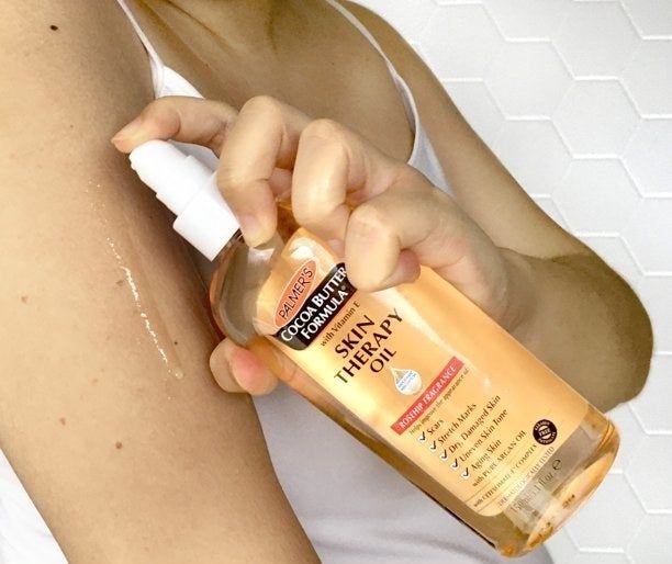 An individual applying oil to their skin for nourishment and hydration.