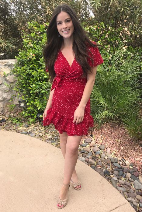 A reviewer, dressed in a red polka-dot dress and sandals, stands outside, smiling at the camera