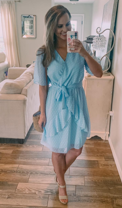 A reviewer in a light blue dress, styled above the knee for a chic, fresh look.
