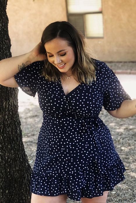 A reviewer is wearing a navy blue polka dot dress