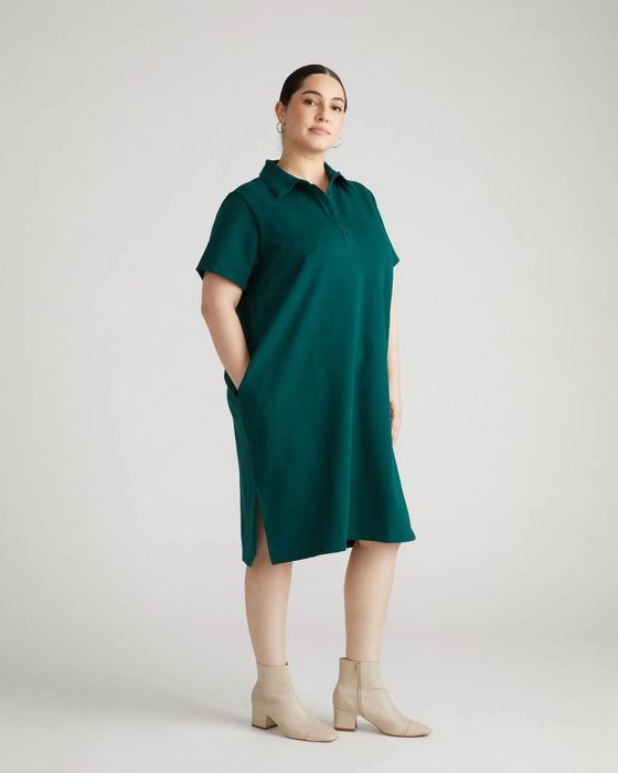 A woman poses in a teal short-sleeve, collared dress featuring pockets, paired with ankle boots.