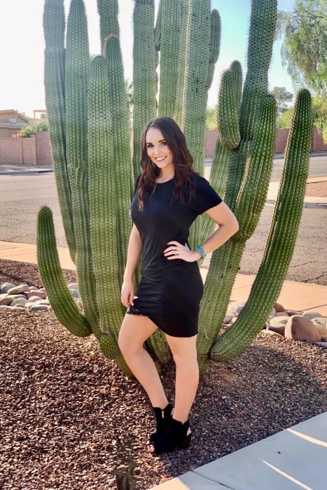 A reviewer is seen wearing a black dress, striking a pose in front of a cactus.