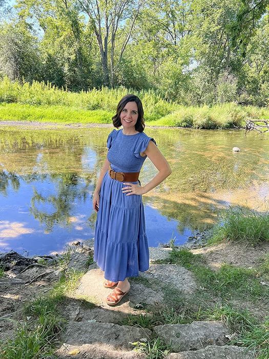The reviewer is wearing a blue dress paired with leather sandals.
