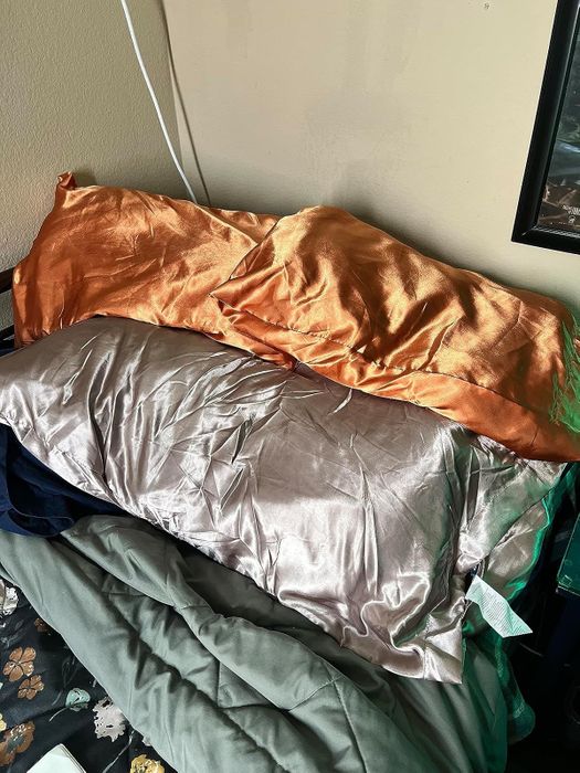 Silk pillowcases on a bed; one in orange and one in silver, arranged atop a green comforter