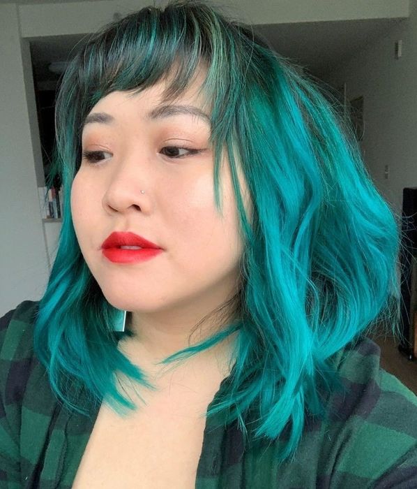 A reviewer with vibrant teal hair that falls to the shoulders