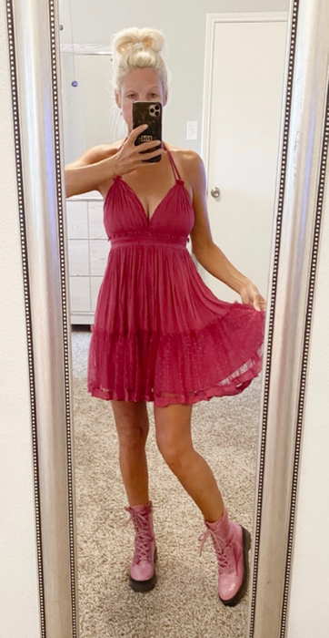 Someone takes a mirror selfie wearing a pink dress with matching boots, their phone covering their face. A pink ribbon symbol is visible in the background.