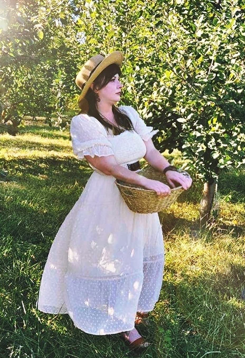 A reviewer in a white ruffled dress standing in a field