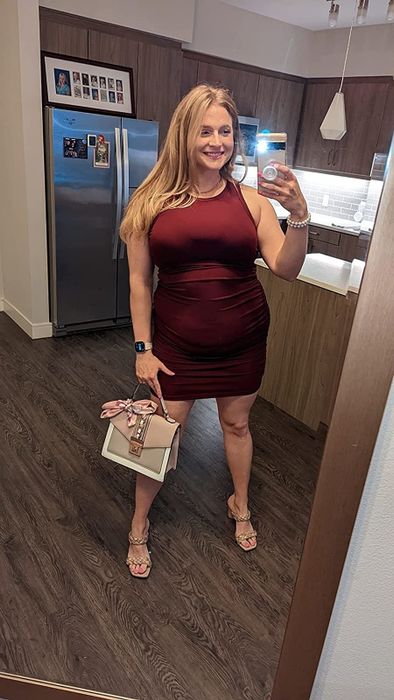 The reviewer is wearing the dress in burgundy, accessorized with heels.