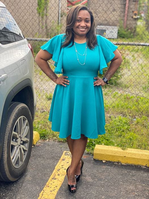 The reviewer is sporting a teal dress paired with black heels.