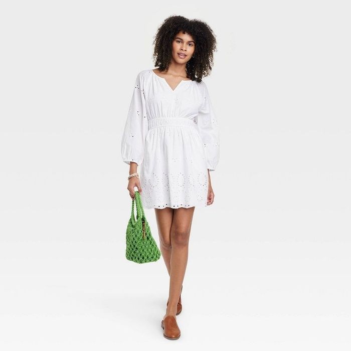 A model wearing the dress in white, paired with a green handbag