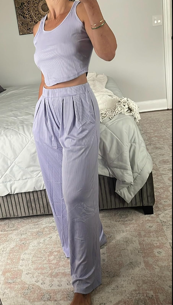 A reviewer wearing a pale purple lounge set featuring a cropped tank top paired with high-waisted, wide elastic pants.