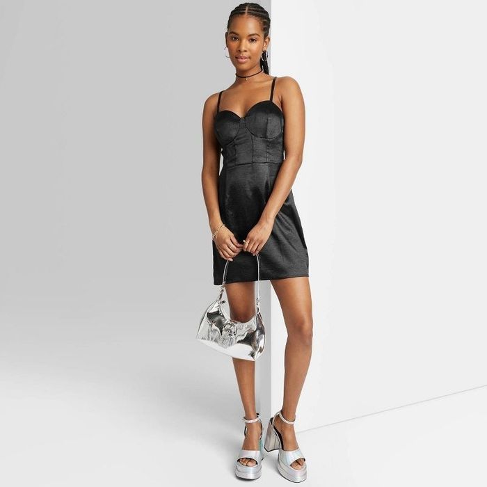 A model wearing a black dress with a silver handbag