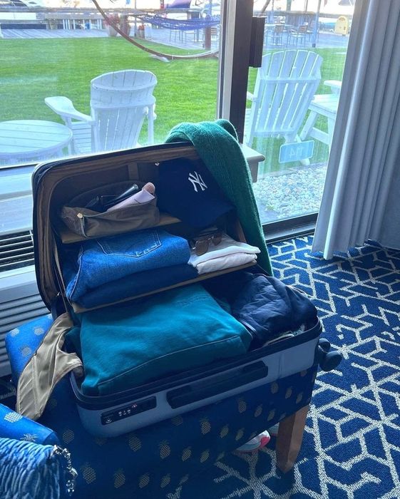 The suitcase displayed in a room filled with clothes, illustrating how the fold-down shelves help keep everything neatly arranged.