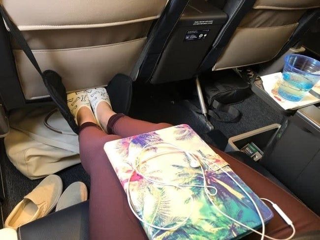 A reviewer’s photo showing a black foot hammock on a plane, with feet comfortably resting inside.