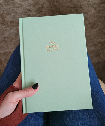 A reviewer holding a green hardcover journal, adorned with a gold-embossed print that reads:
