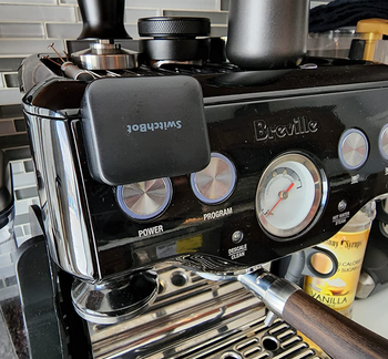 The black version of the SwitchBot on a coffee machine button.
