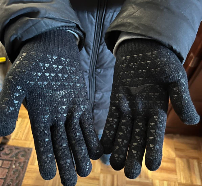 Black touchscreen gloves with textured indentations on the fingers, worn by a reviewer