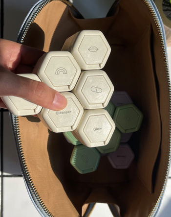 A hand pulls out a stack of white capsules, all neatly arranged together, from a cosmetics bag.