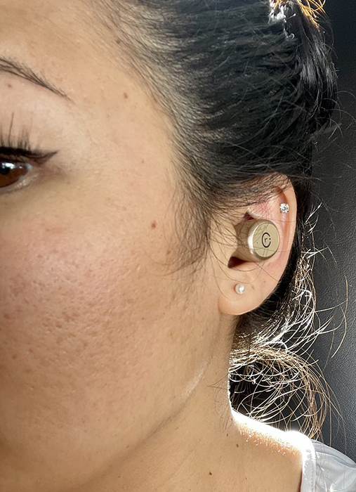A reviewer is shown wearing the rose gold earbuds in their ear.