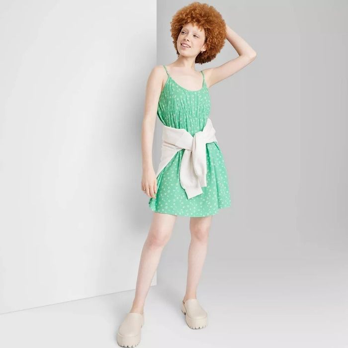 A model wearing a sleeveless green babydoll mini dress with white floral details