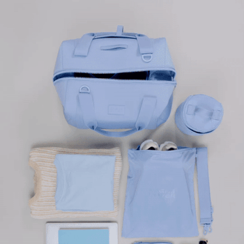 A gif of a model demonstrating how much the duffle bag can hold while packing it up