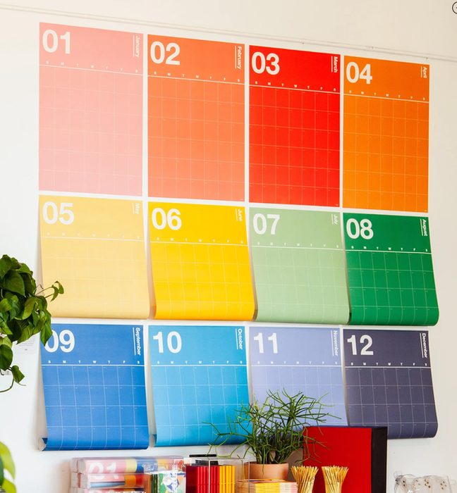 A 12-month undated calendar, each month displayed on a separate, colorful page hanging in rainbow hues on the wall.