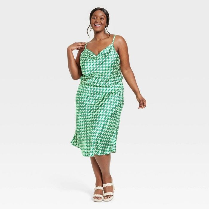 A model showcasing the dress in a green geometric pattern paired with white shoes