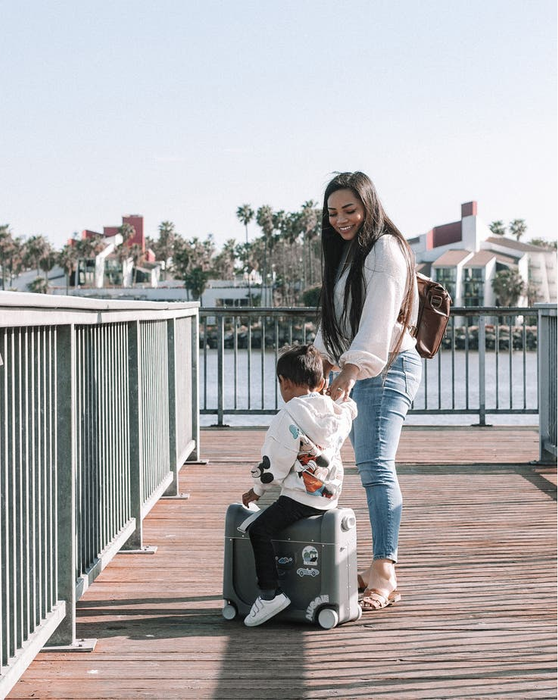 a child model riding the wheeled suitcase while an adult model pulls them beside it