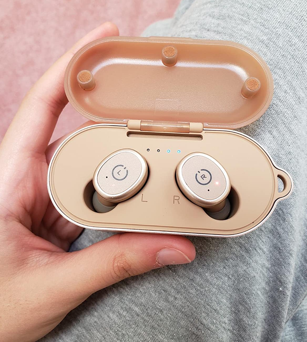 A reviewer holds the rose gold earbuds in their charging case.