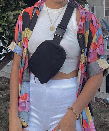 A reviewer sporting a black fanny pack with buckles, worn across their shoulder and chest.