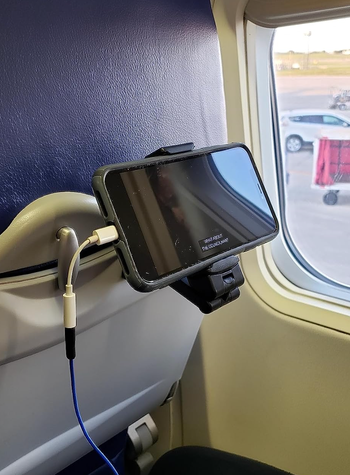 A phone securely attached to the back of an airplane tray table using a black clip device